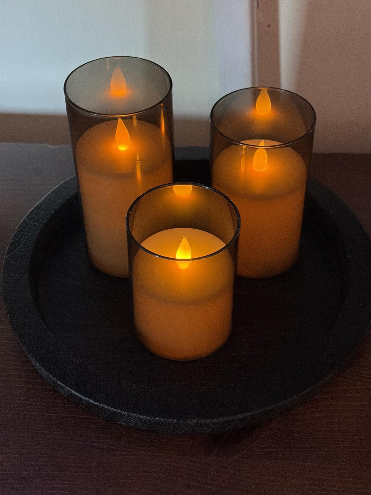 Three flameless glass candles glowing on a black tray